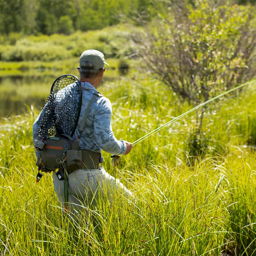 816332015694 EHLP-P Fishpond Elkhorn Lumbar Pack Pebble New Fishpond Waist Pack Front Walking Through Grass Near A River