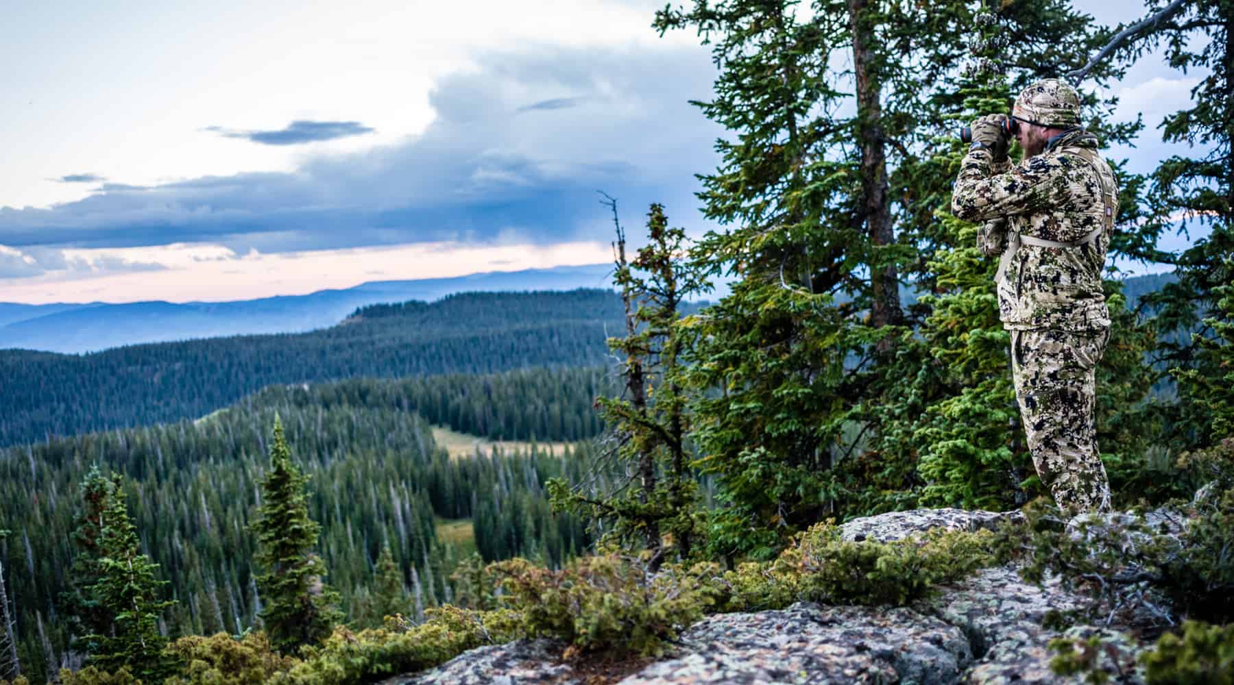 Sitka Gear Sale Header - Man in Sitka Clothing (Optifade Camoflauge) Using Binoculars to Scan the Forest